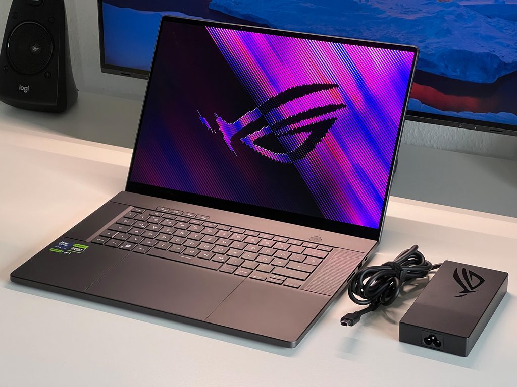 Black ASUS ROG Zephyrus G16 laptop open next to its power adapter and retail box