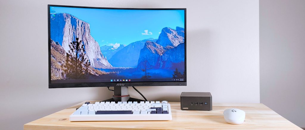 ASUS NUC 14 Pro mini PC sitting next to a white monitor on a modern desk setup.