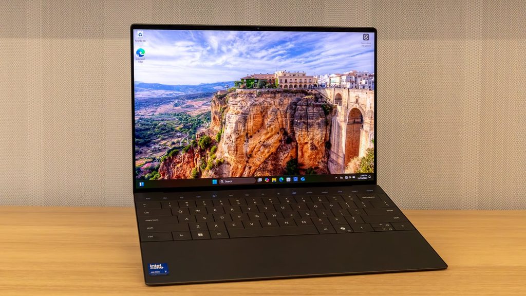 Black Dell XPS 13 slim laptop open on a wooden table showing Windows desktop