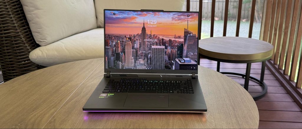 ASUS ROG Strix G16 gaming laptop open on a wooden table with RGB light bar illuminated