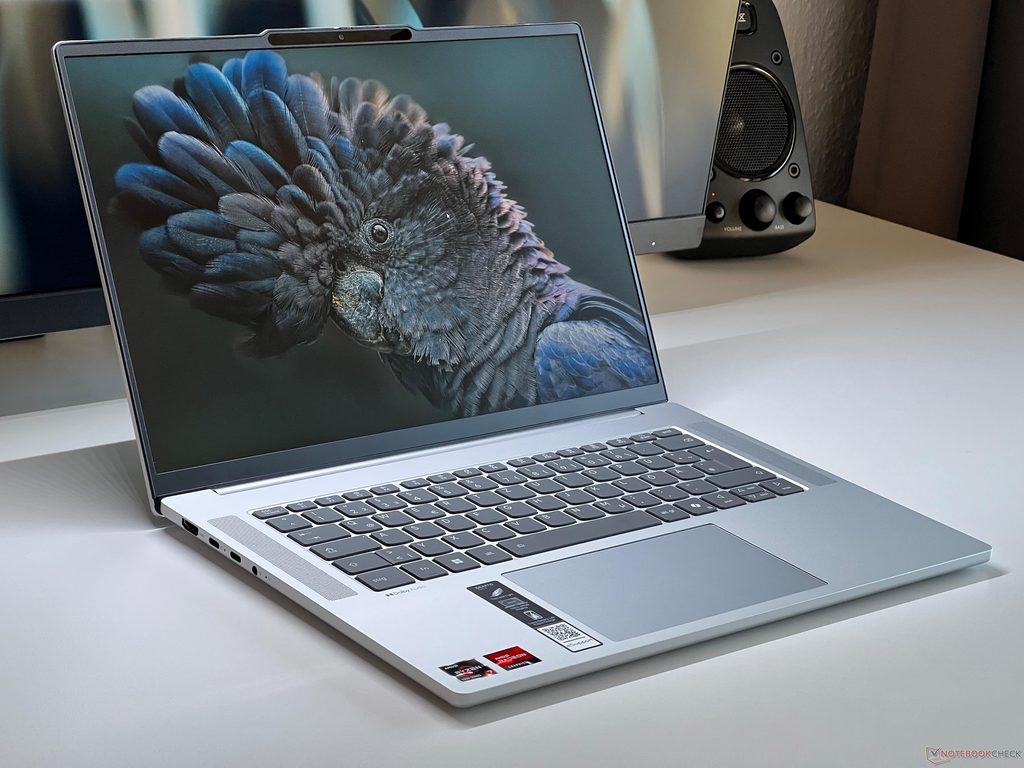 Grey Lenovo IdeaPad Slim 5 laptop open on a table showing a bird wallpaper next to a speaker